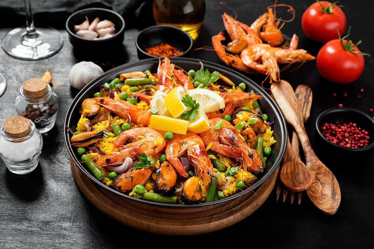 Image of beautifully served and presented paella along with spices, salt, pepper and tomato on the table