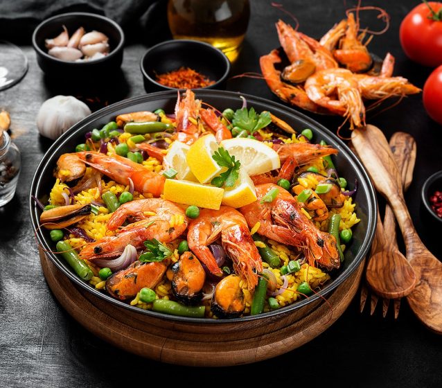 Image of beautifully served and presented paella along with spices, salt, pepper and tomato on the table