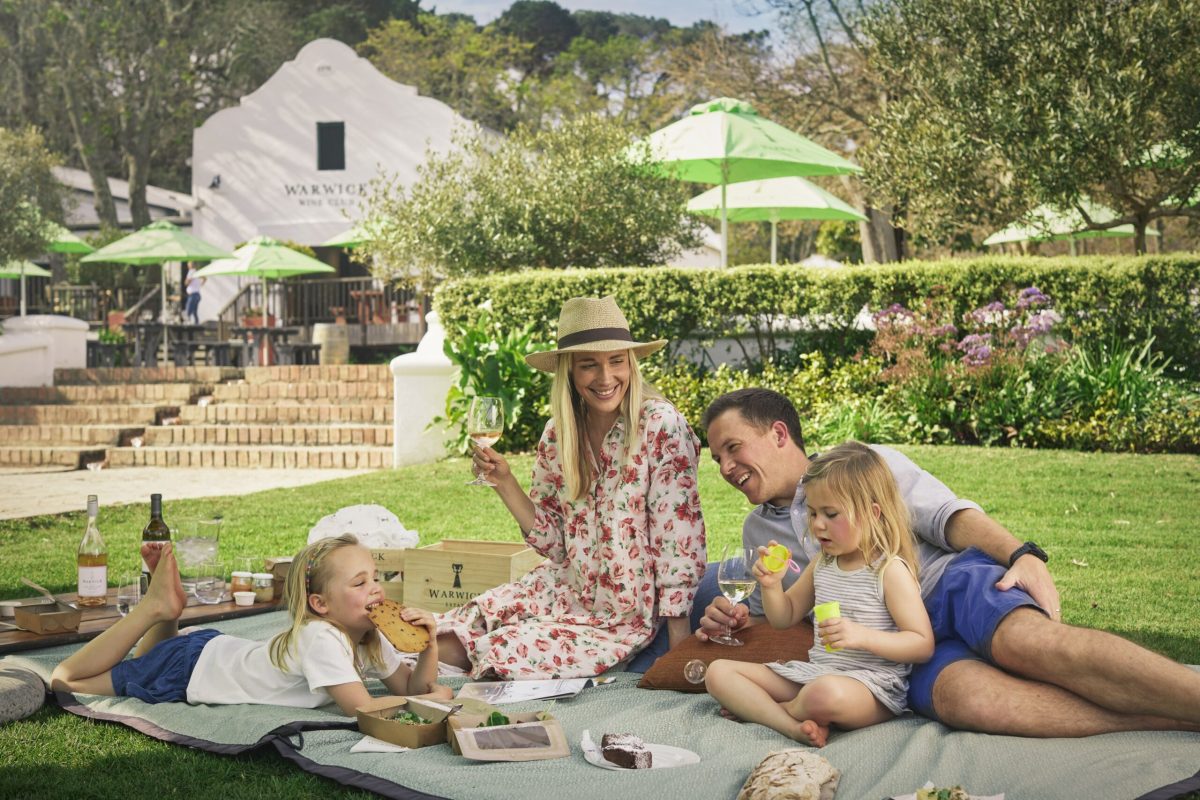 Image of wife and husband with children siting on a lawn at enjoying picnic at Warwick Estate